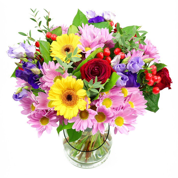 This image shows a lush mixed bouquet poised in a cylindrical glass vase, set before a white background that lets every petal and leaf take centre stage. The design is generous and rounded, with the blooms arranged so that no side feels heavier than another, much like a balanced table arrangement ready for a family gathering in Abbots Langley. At the core, deep red roses form a romantic heart, their petals layered into tight spirals that draw the eye inward. Radiating from this centre, two golden yellow gerbera daisies with warm, brownish-orange eyes bring an immediate sense of joy and brightness, their flat, symmetrical faces standing proudly among the other stems. Around them, a halo of soft pink and lavender daisy-like chrysanthemums spreads outward, each flower composed of countless slender petals tipped in gentle colour, their small yellow centres adding a subtle, sunlit glow. Interspersed among the daisies, you can see elegant lisianthus blooms in rich purple and softer lilac hues, their slightly curled, bell-shaped petals lending a touch of sophistication and cool contrast to the warmer tones. Small clusters of round, shiny red Hypericum berries punctuate the bouquet like tiny ornaments, adding depth and an almost festive feel. Embracing all the blooms is an abundance of green foliage, from strong, dark leaves that ground the arrangement to lighter, more delicate sprigs that reach outward, giving movement and a freshly gathered-from-the-garden impression, reminiscent of nearby open spaces around Leavesden. Through the transparent vase, the neatly aligned stems are visible in clear water, underscoring the care and skill of the florist who created it. The overall effect is one of happy celebration and sincere sentiment, ideal for marking birthdays, anniversaries, or everyday acts of kindness in Abbots Langley.